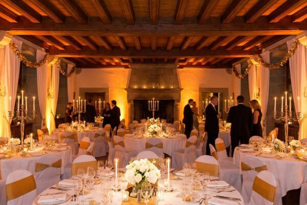 Festlich dekorierter Bankettsaal mit weissen Tischdecken, Kerzenlicht und Blumenarrangements unter Holzbalkendecke