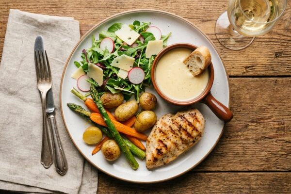 Mittagsteller mit grilliertem Poulet, Ofenkartoffeln, Spargeln und Rucola-Salat auf Holztisch
